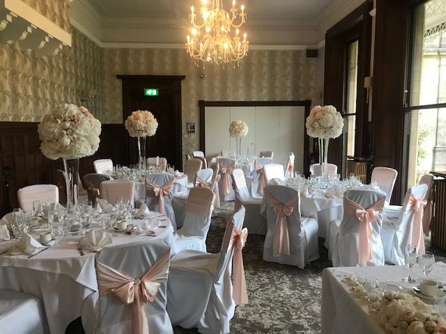 The combination of white table decorations with elegant touches of pastel pink bows on the chairs and roses in the middle of the tables.