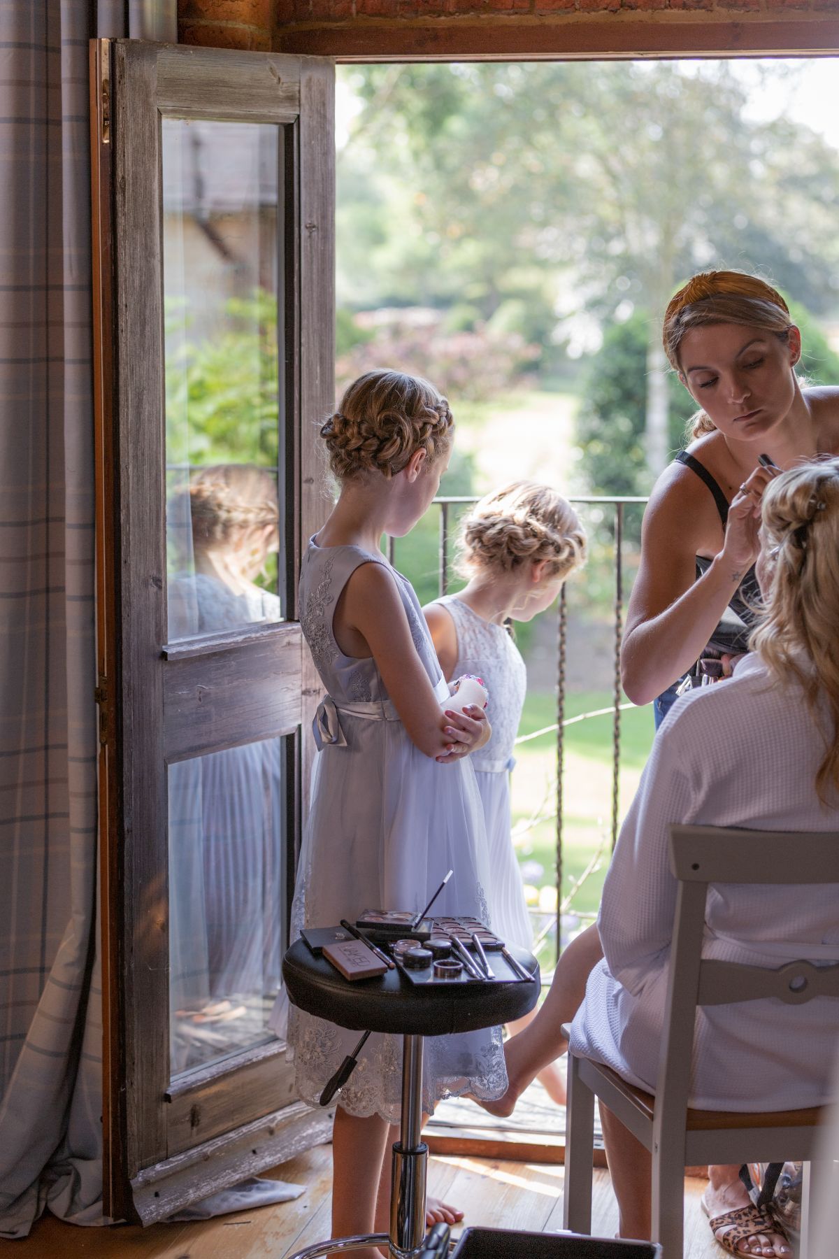 Brides preparations with flower girls looking on.