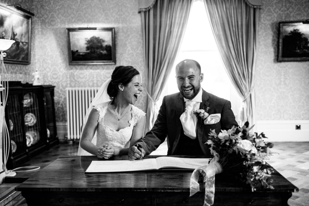 Bride and Groom hear something funny in the background as they sign the register at The Mount Ephraim Gardens