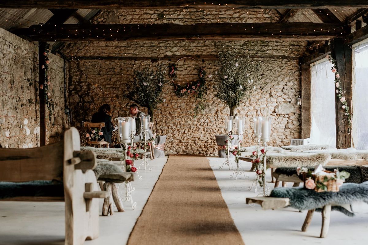 Ceremony in the Stone barn with blush flowers, faux fur throws and rustic wooden benches