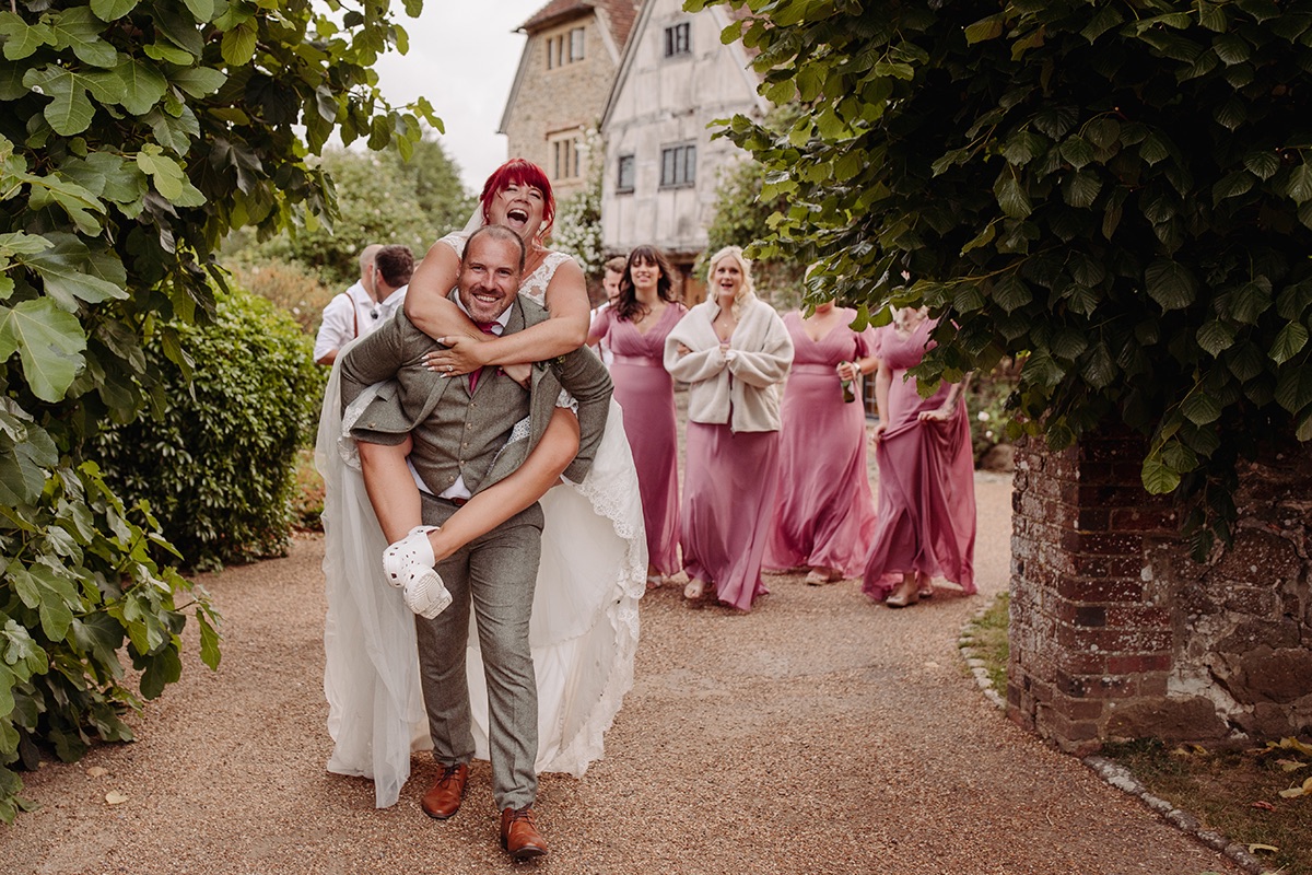 Groom gives bride a piggy back at their Grittenham Barn wedding 