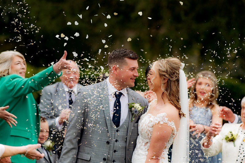 Lucy & Jordan in the grounds of Carr bank whilst guests throw confetti at Carr Bank Wedding Venue Mansfield Nottinghamshire 