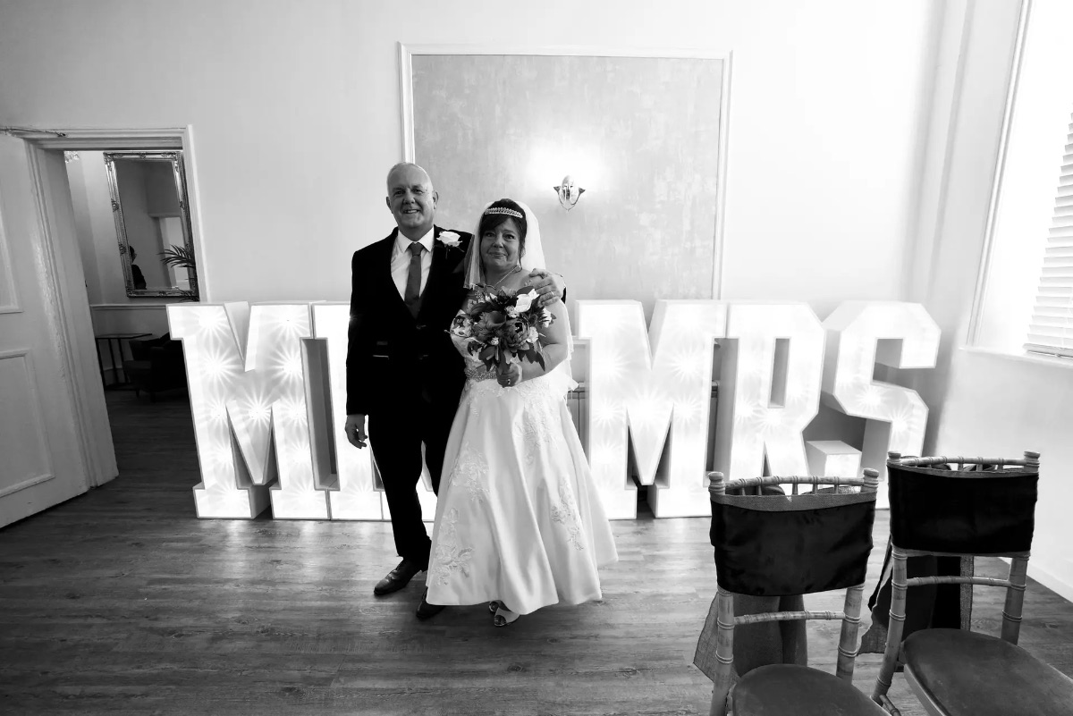 Nicola & Mark stood in front of the huge MR&MRS iluminated letters the ceremony room at Carr Bank Wedding Venue Mansfield Nottinghamshire 