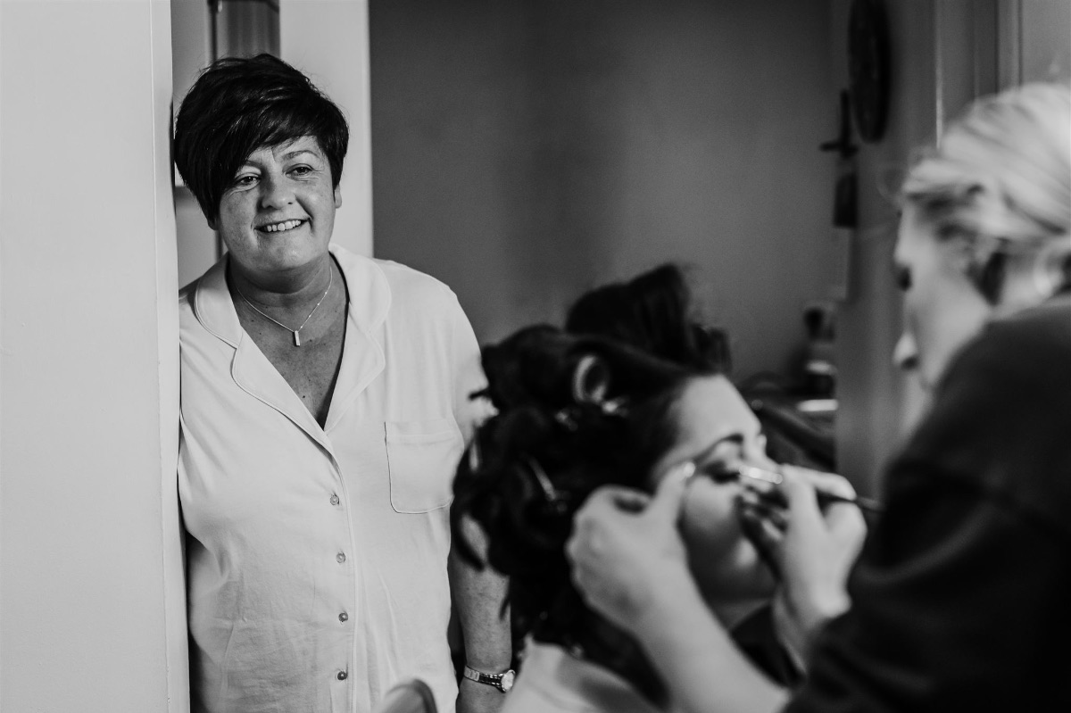 mother of the bride watches her daughter get her bridal make applied