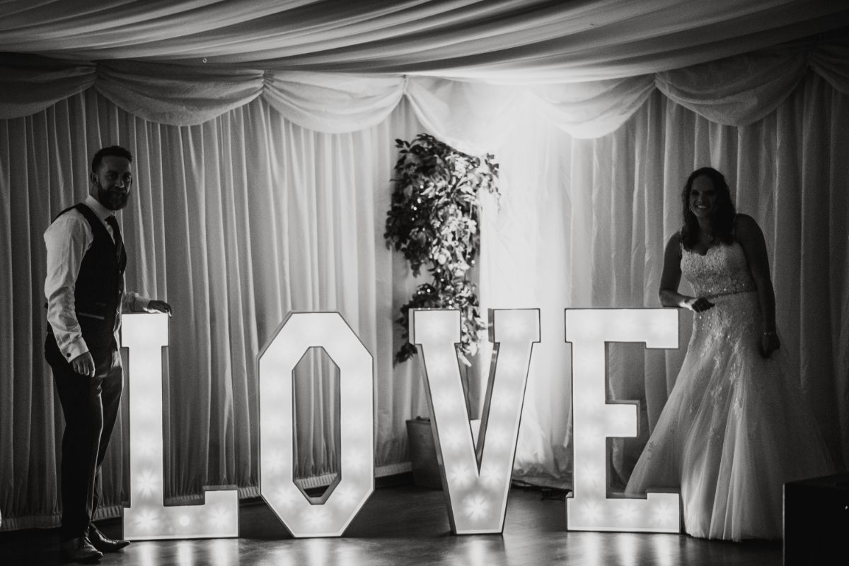 Bride and groom posing next to LOVE letters in Marquee 