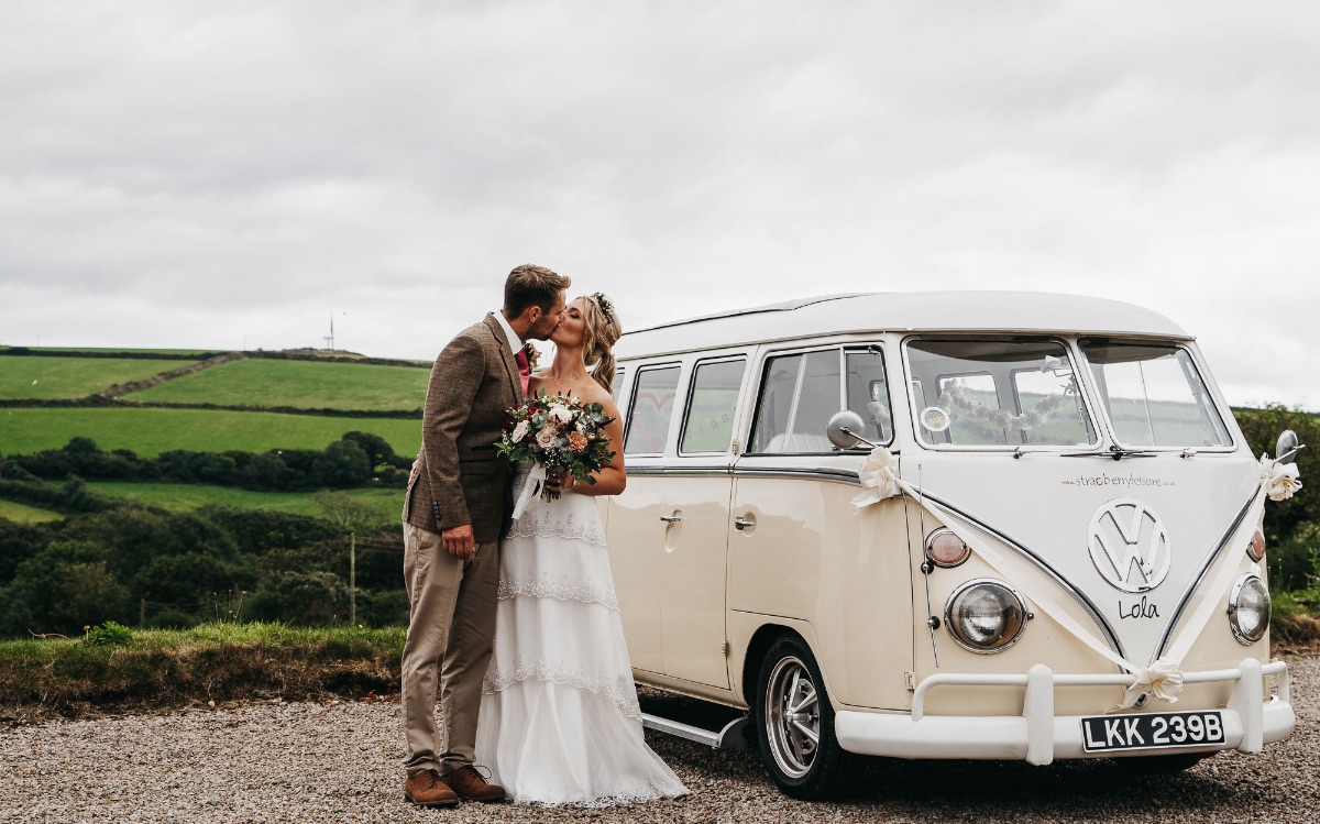 Bride and groom kiss next to their wedding van